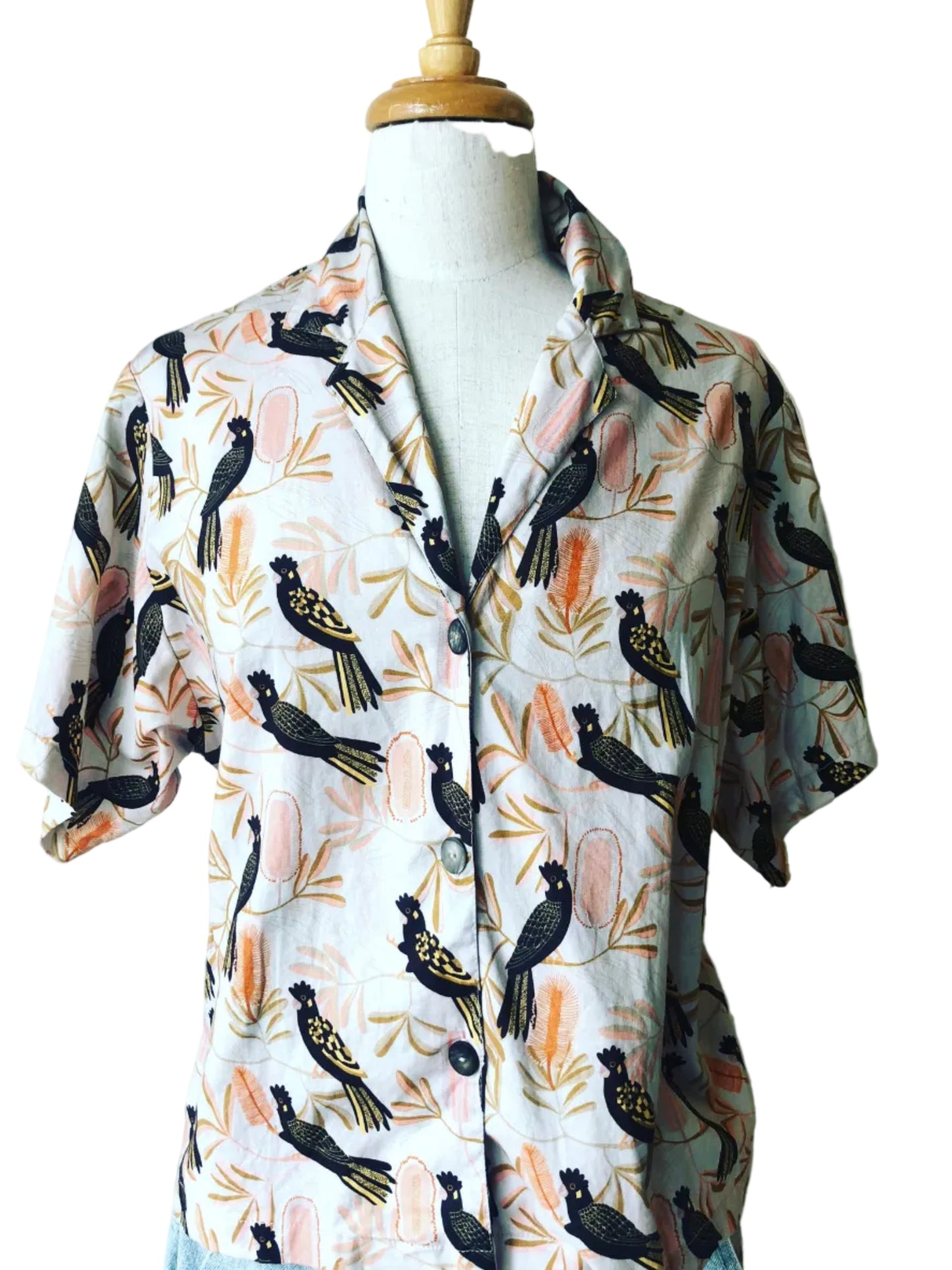 A crop bobby shirt with a blush pink background featuring black cockatoo prints.