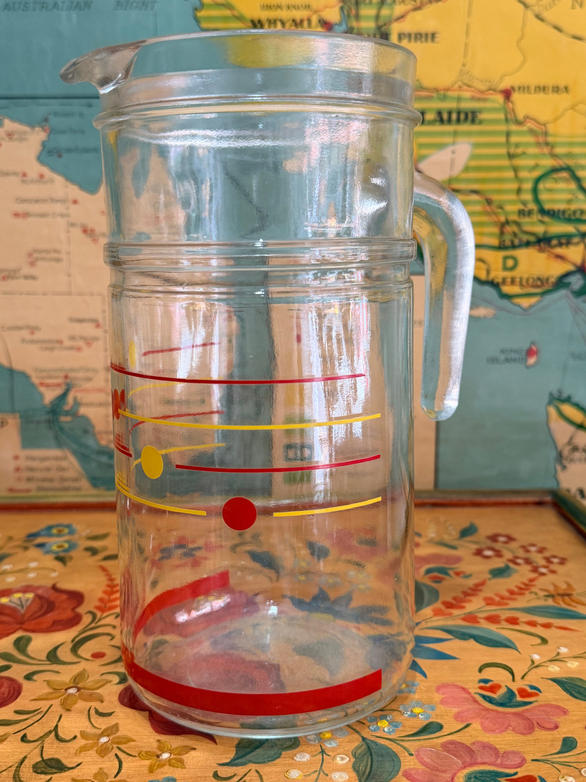 A set of retro clear glass drinking ware, including a large pitcher and six tumblers, decorated with red and yellow polka dots,