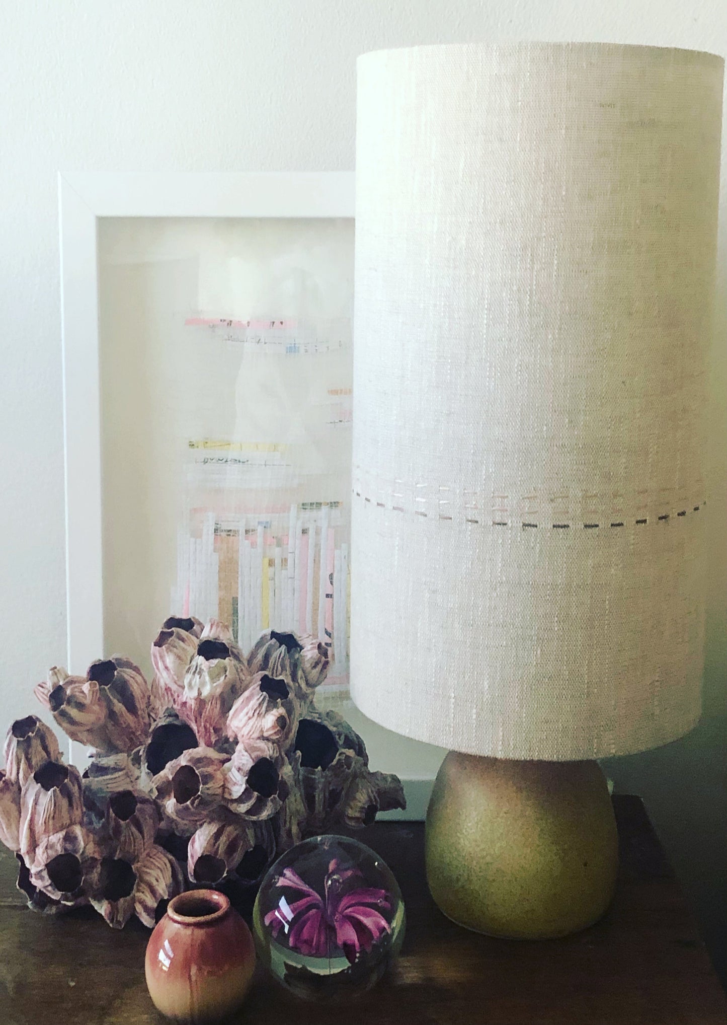 Decorative lamp with a textured white shade on a table next to a floral arrangement and small decorative items.