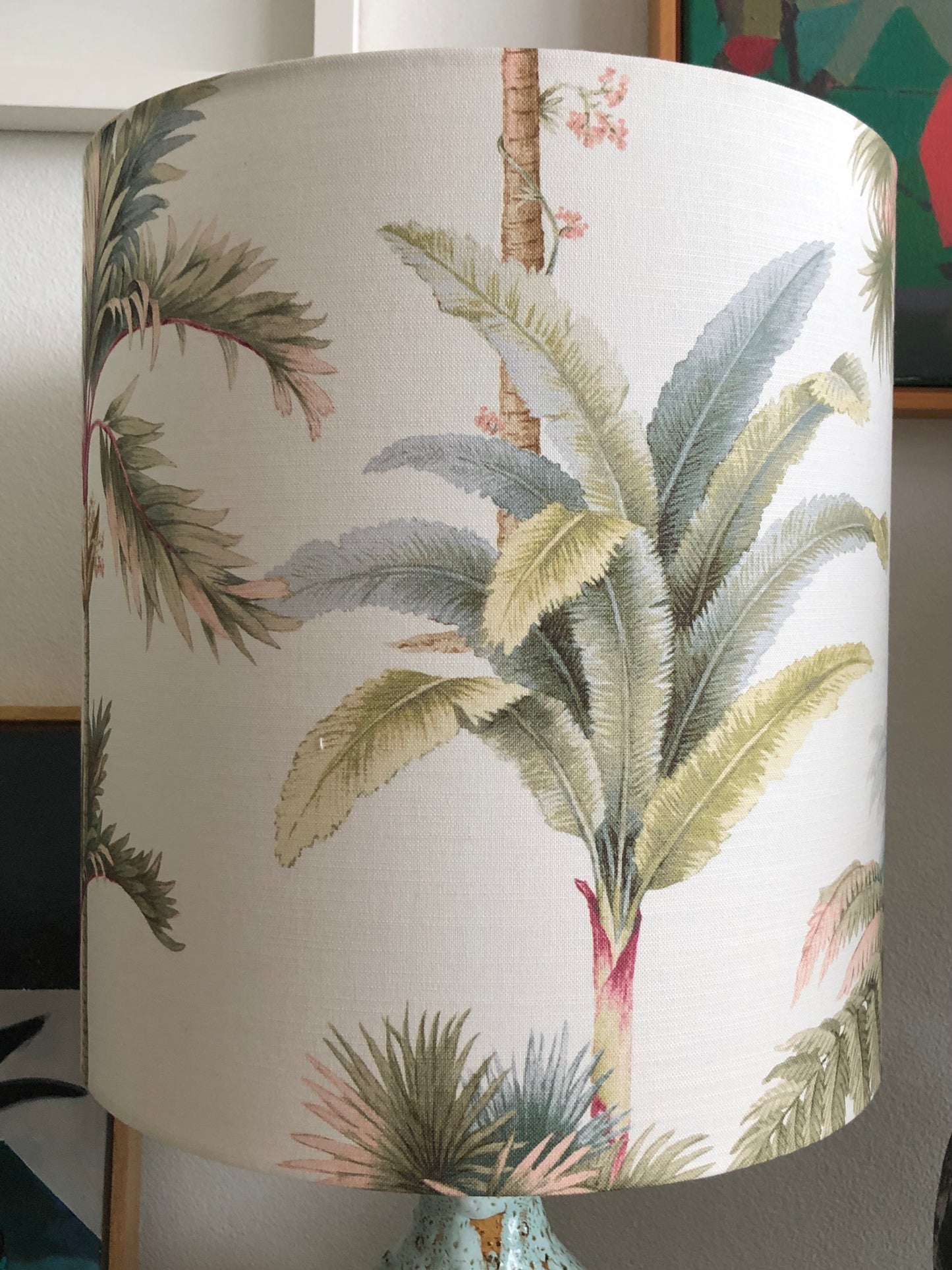 A blush pink vintage palm lampshade with green palm designs, displayed on a lamp.