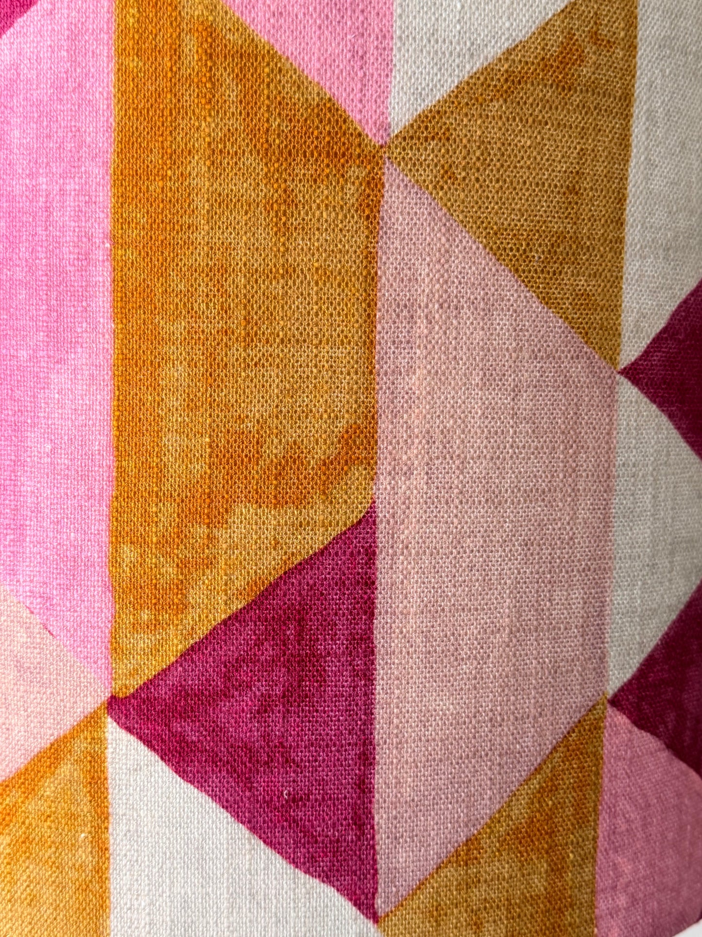 A close-up of a woven textile with a geometric triangle pattern in pink, mustard yellow, cream, and magenta.