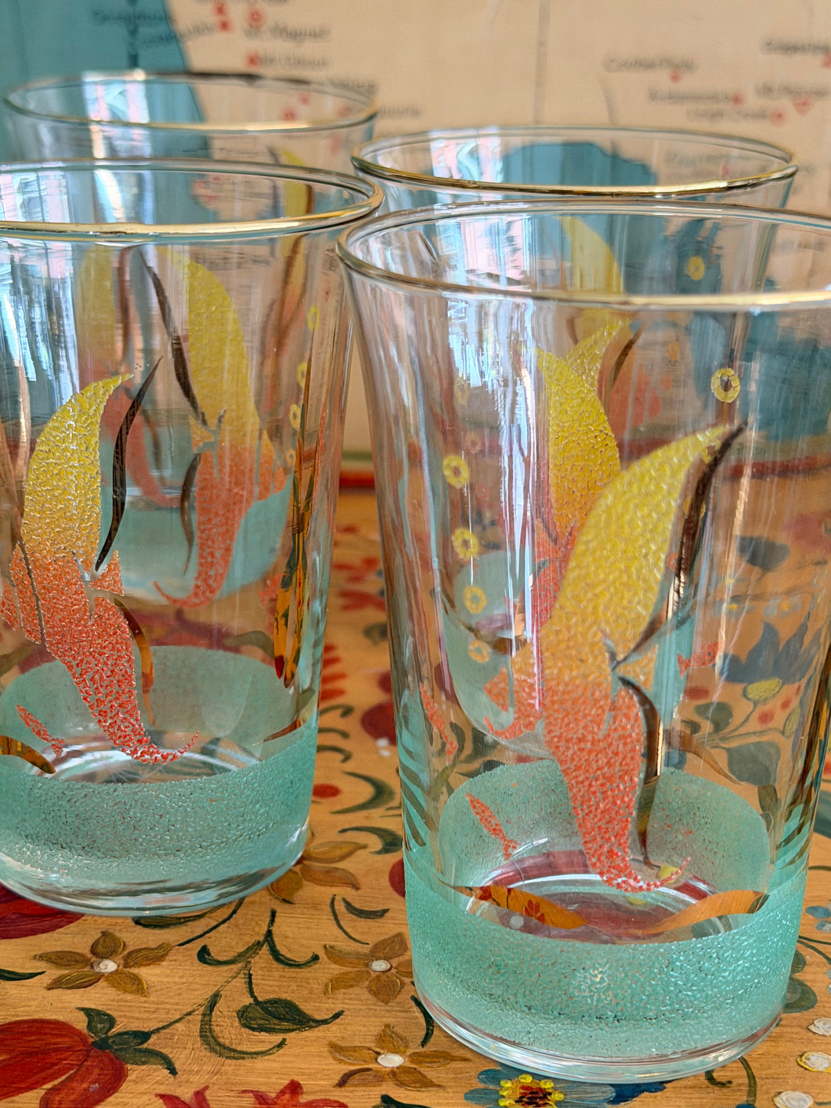 A retro frosted pitcher with fotumblers, decorated with colorful fish illustrations in yellow, orange, and red and with a sea green frosted band