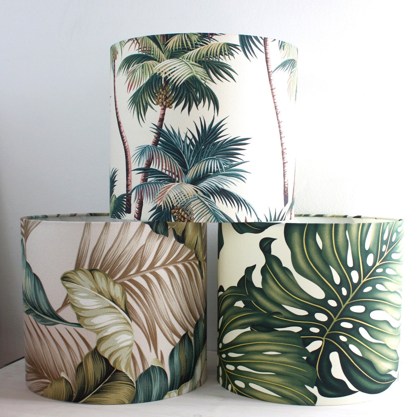 A collection of three lampshades with monstera palm leaf prints in different sizes, displayed from largest to smallest.
