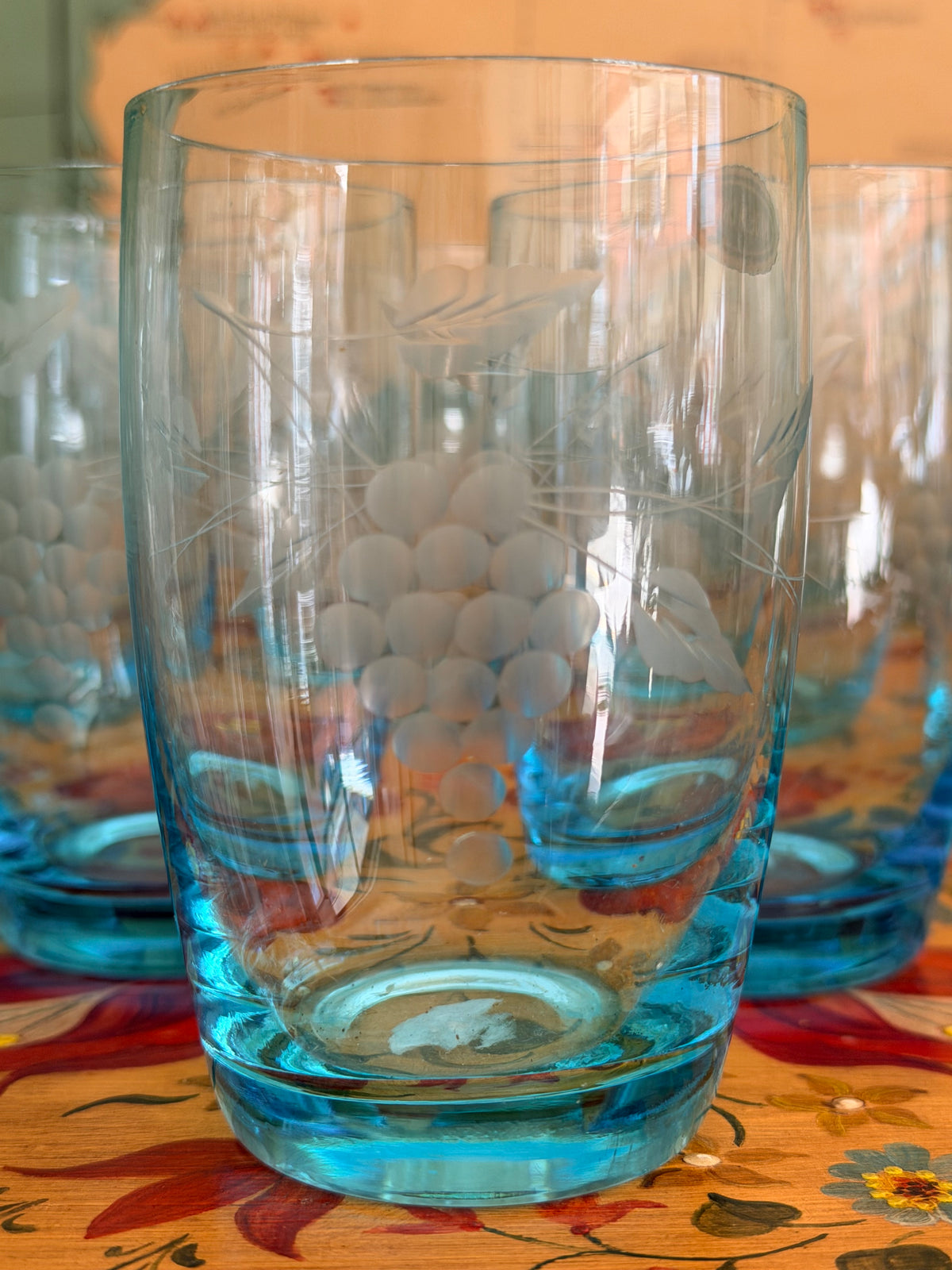 A group of retro vintage aqua blue glass tumblers with etched grape designs and bright blue bases,