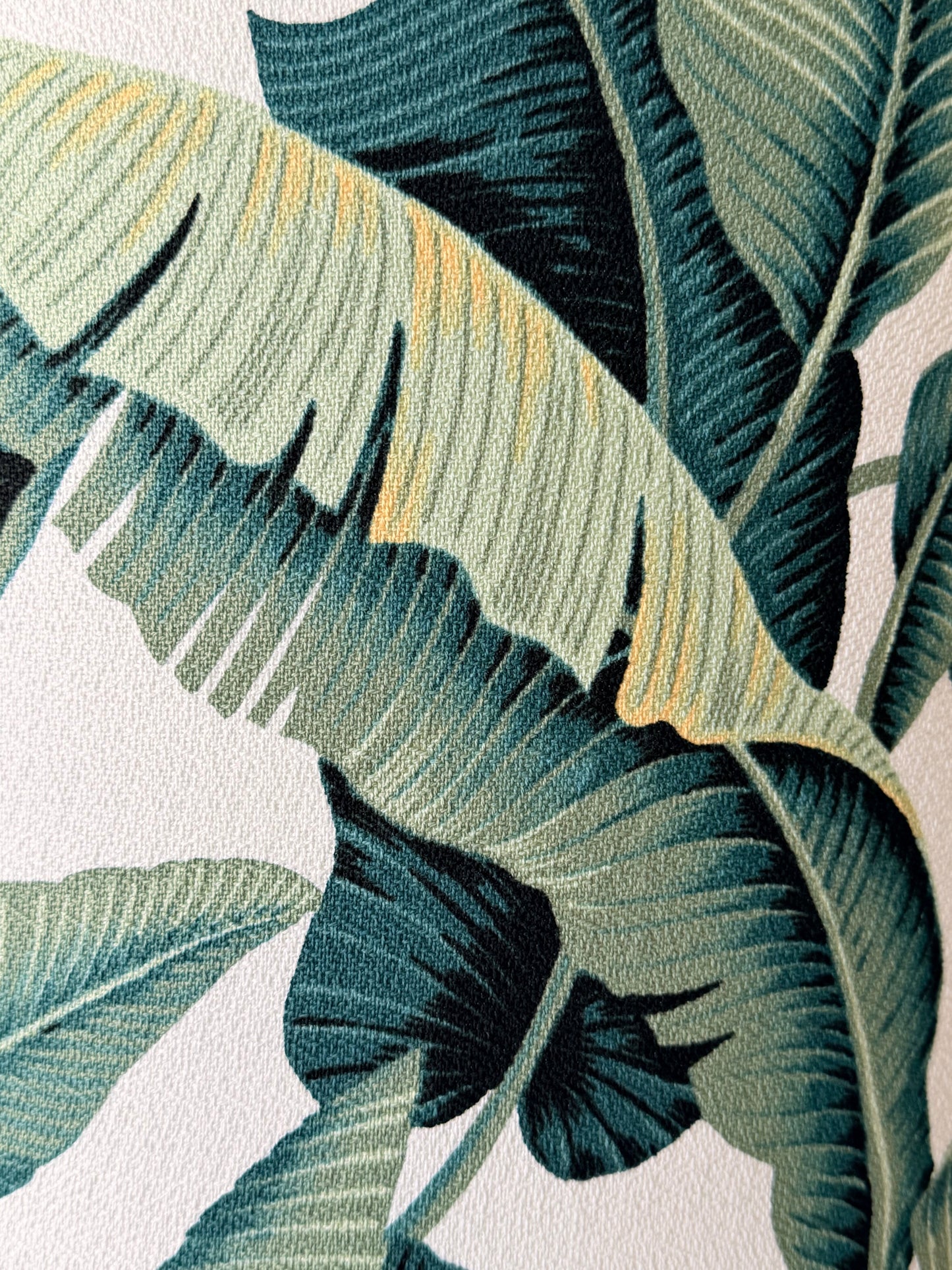 Close-up of a tropical leaf pattern with large banana-leaf-like shapes in dark teal, green, and muted yellow on a white background.