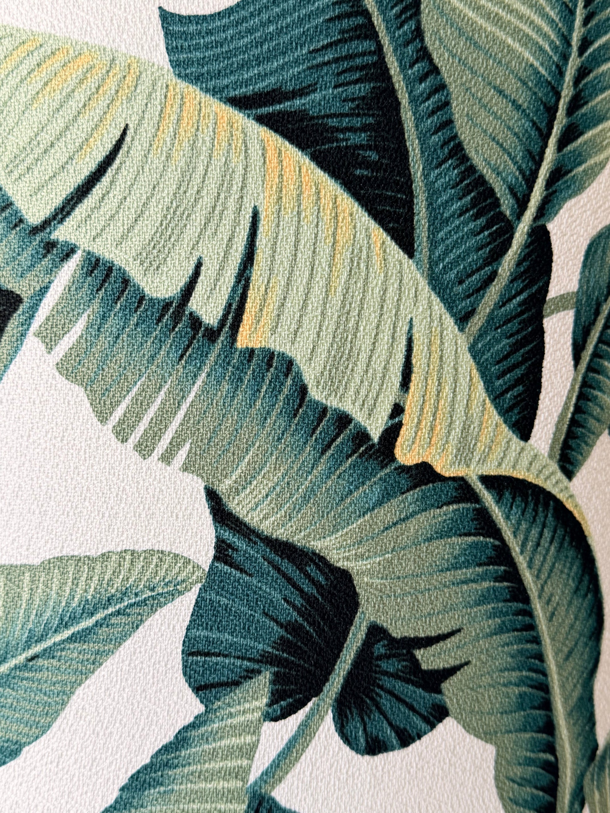 Close-up of a tropical leaf pattern with large banana-leaf-like shapes in dark teal, green, and muted yellow on a white background.
