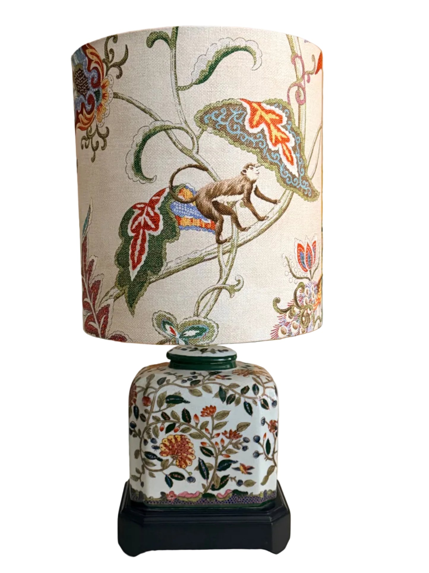 A pair of vintage-style table lamps with white fabric drum shades featuring a colorful botanical and animal print, and matching white ceramic jar bases with floral patterns