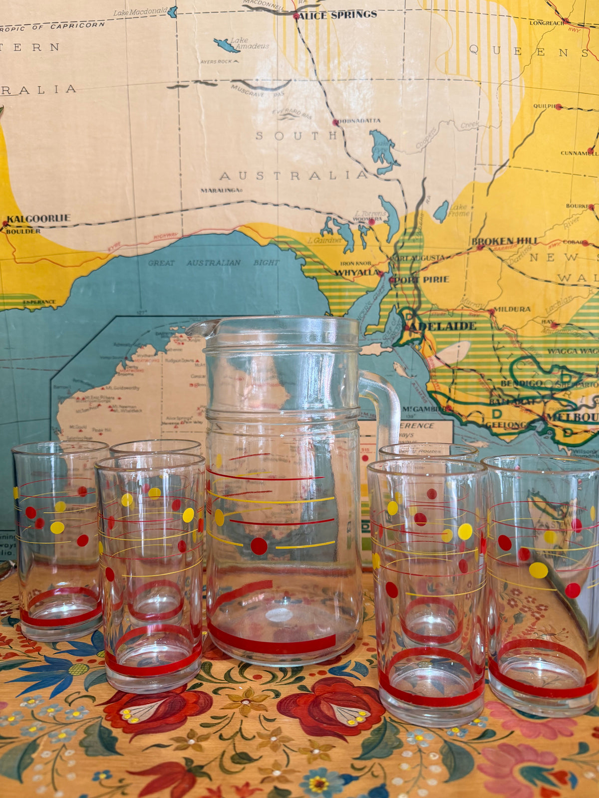 A set of retro clear glass drinking ware, including a large pitcher and six tumblers, decorated with red and yellow polka dots, 