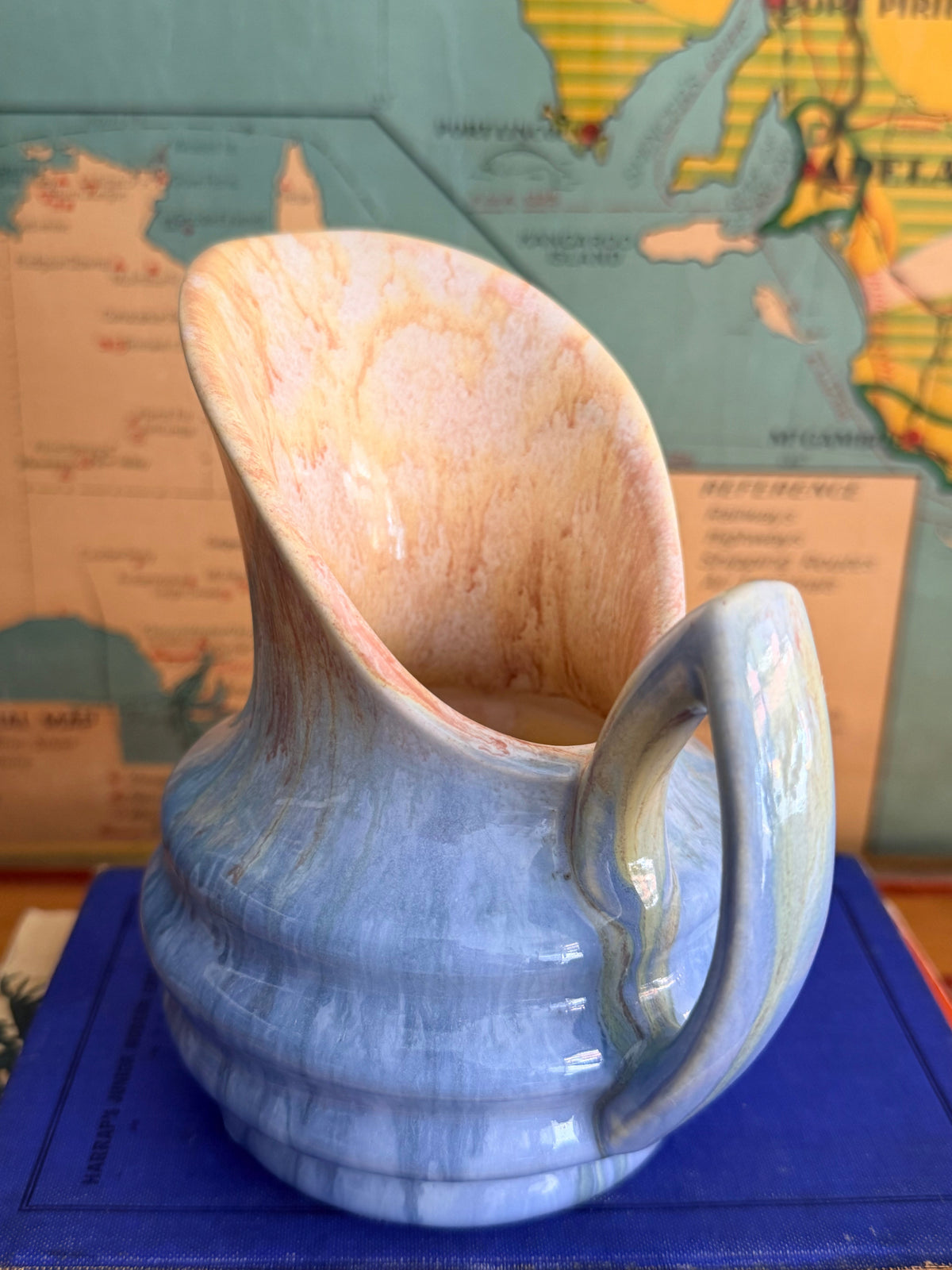 A small ceramic pitcher with a blue and beige marbled drip glaze