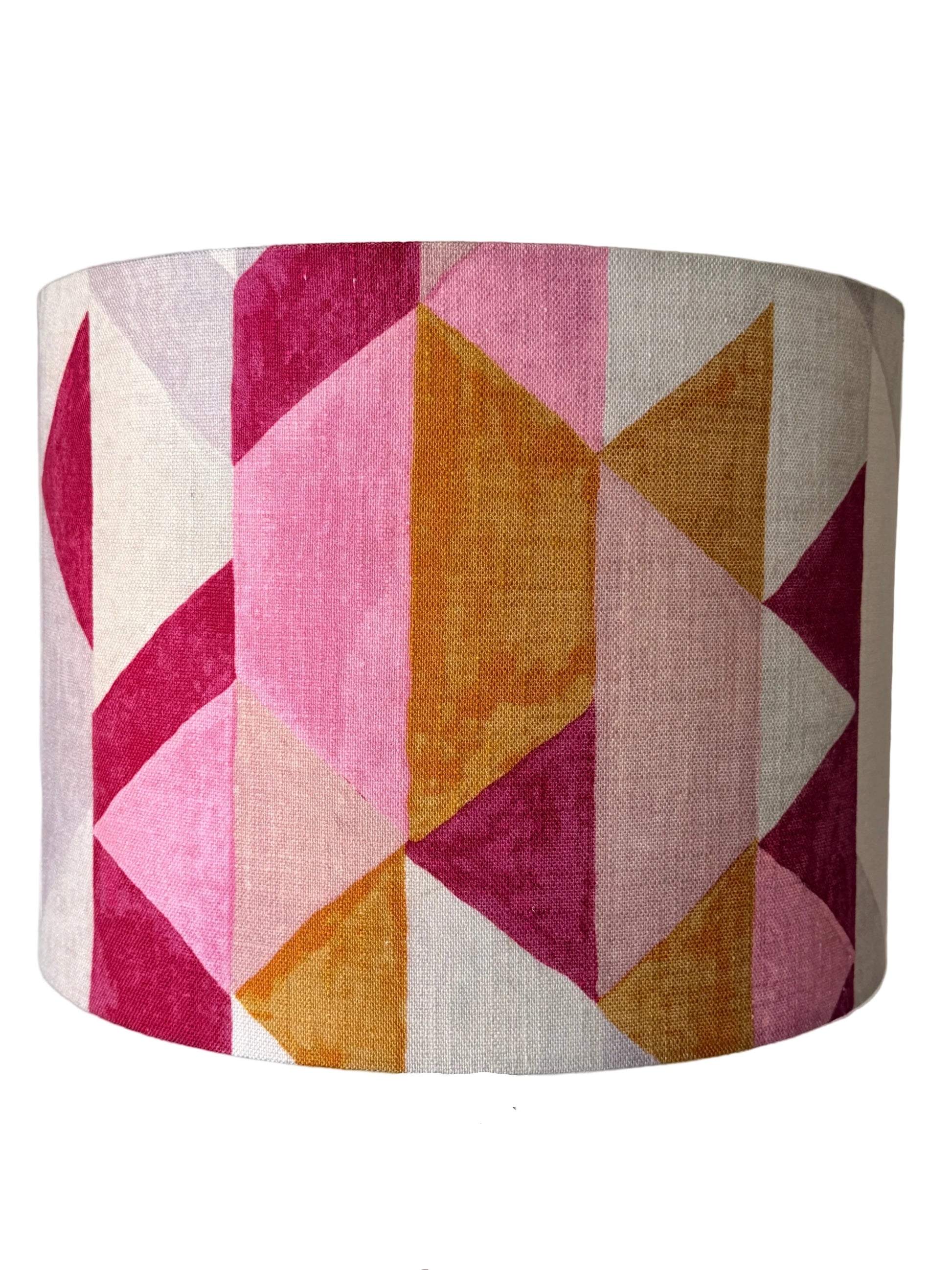 A drum lampshade with a geometric pattern of pink, magenta, ochre orange, and cream linen-textured triangles