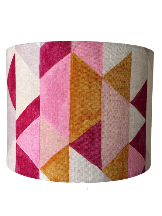 A drum lampshade with a geometric pattern of pink, magenta, ochre orange, and cream linen-textured triangles