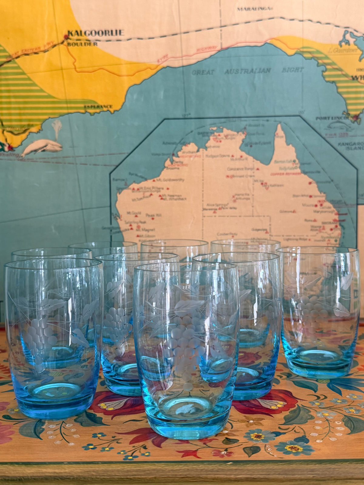 A group of retro vintage aqua blue glass tumblers with etched grape designs and bright blue bases,