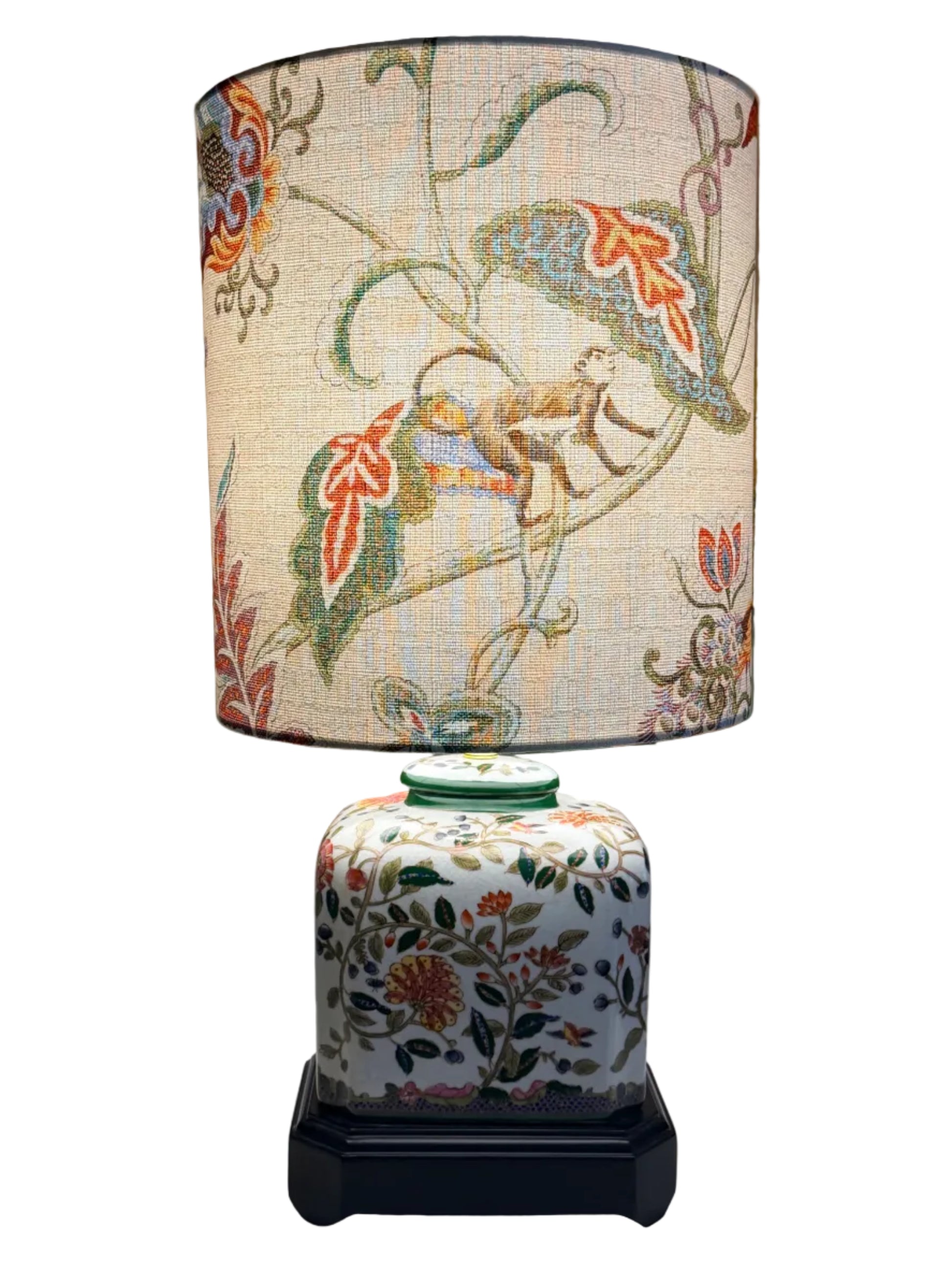 A pair of vintage-style table lamps with white fabric drum shades featuring a colorful botanical and animal print, and matching white ceramic jar bases with floral patterns