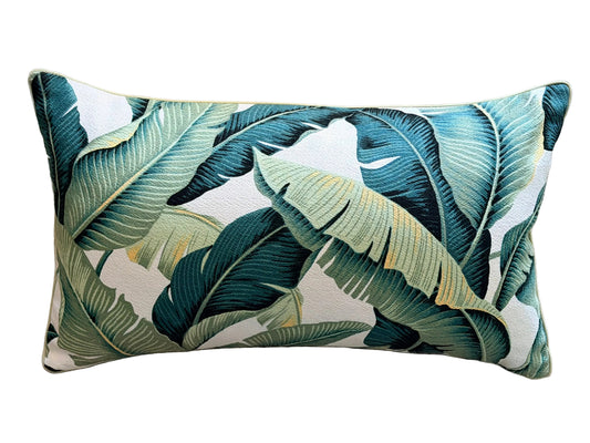 A rectangular lumbar throw pillow with a tropical banana leaf pattern in teal, green, and cream