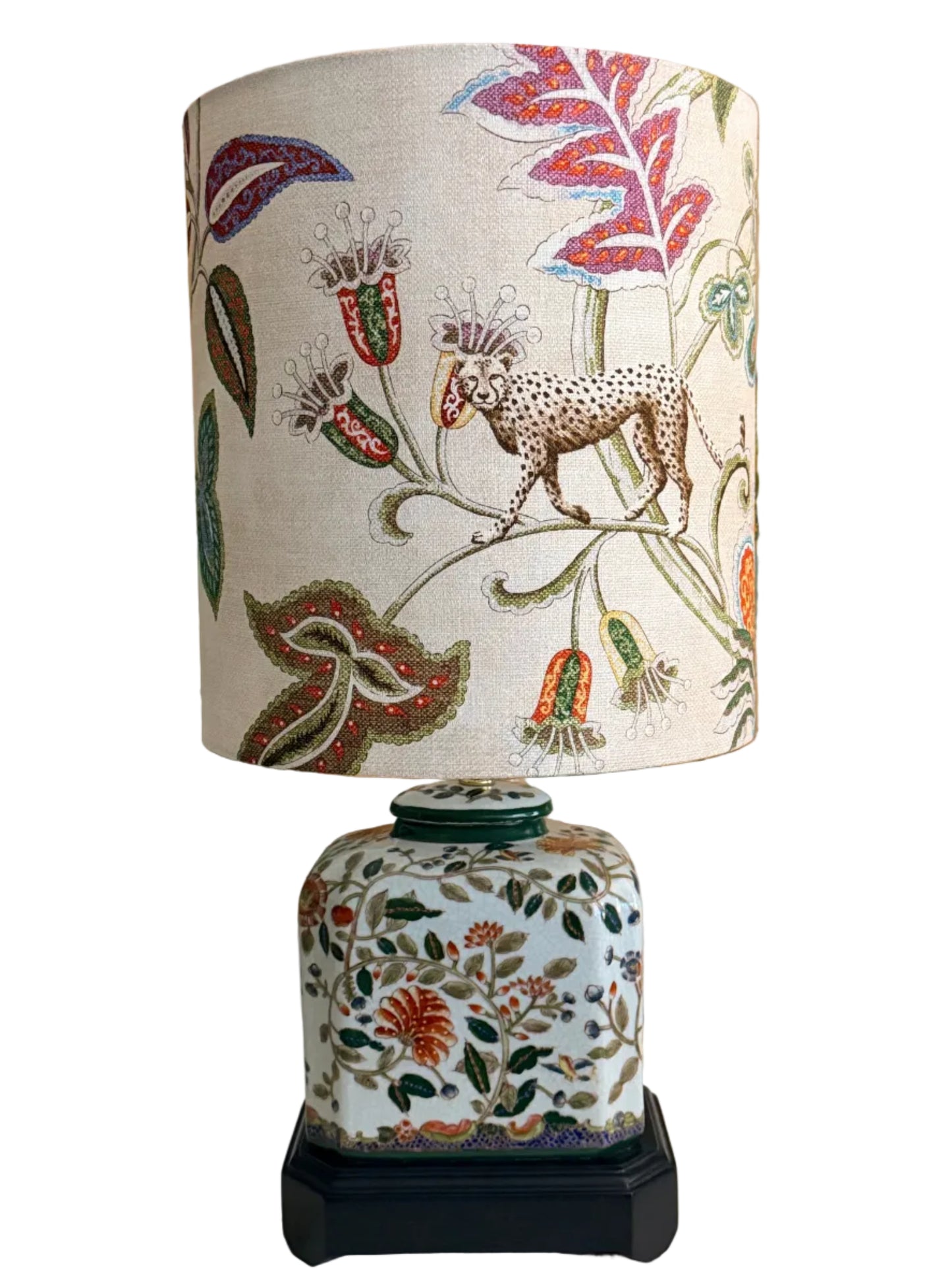 A pair of vintage-style table lamps with white fabric drum shades featuring a colorful botanical and animal print, and matching white ceramic jar bases with floral patterns