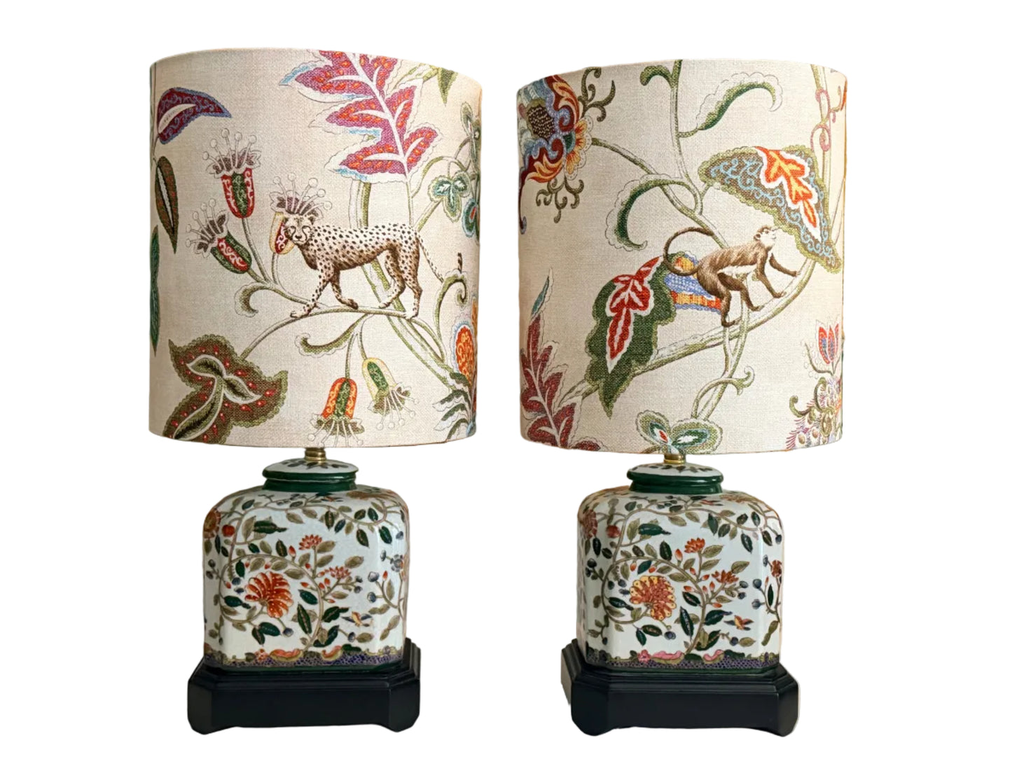 A pair of vintage-style table lamps with white fabric drum shades featuring a colorful botanical and animal print, and matching white ceramic jar bases with floral patterns