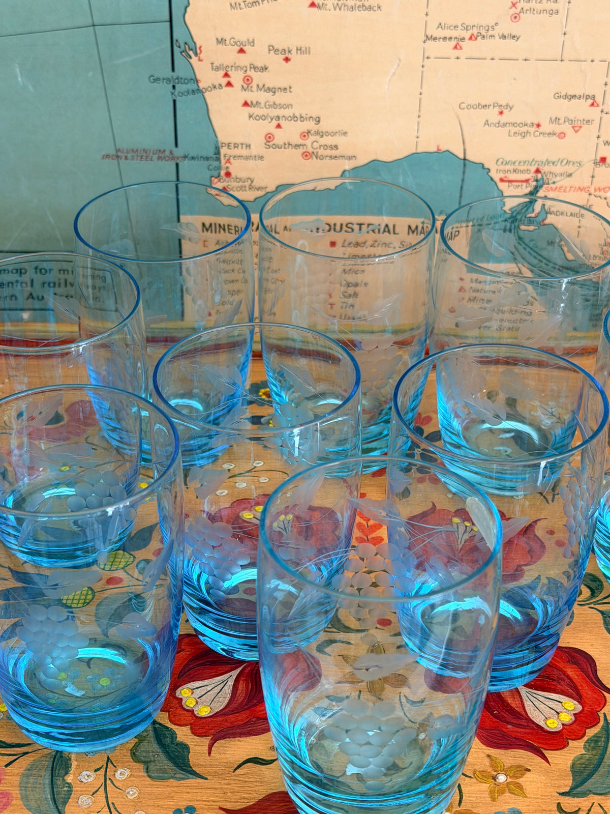 A group of retro vintage aqua blue glass tumblers with etched grape designs and bright blue bases,