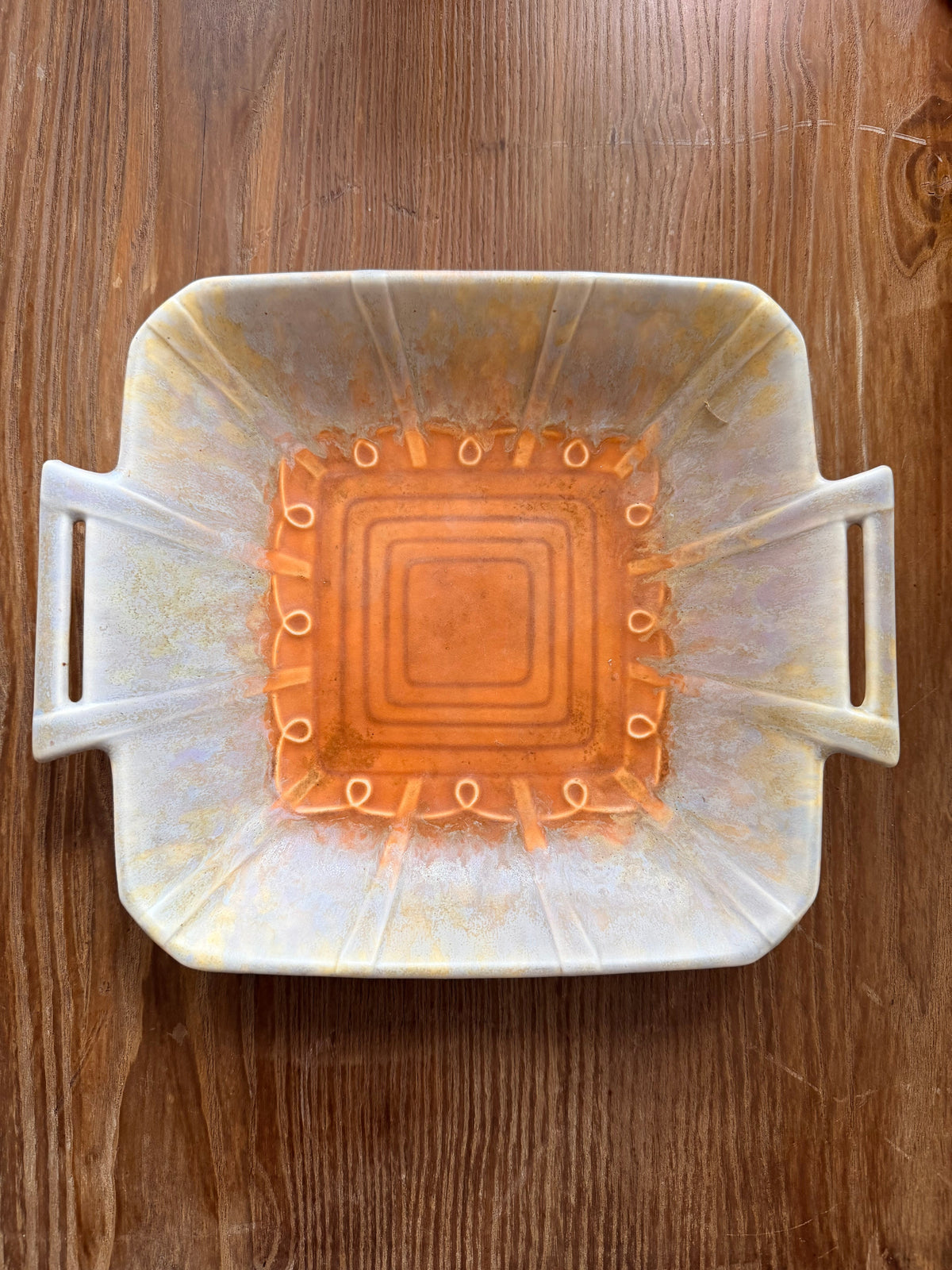 A beswick plate with side handles, featuring a taupe exterior with subtle yellow speckles and a vibrant  burnt orange interior with concentric square patterns and small circular details.