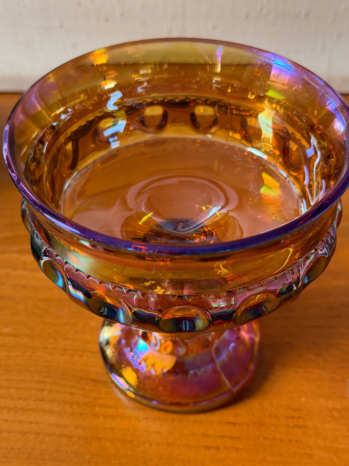 An iridescent carnival glass pedestal bowl , compote, with a gold-amber base and rainbow reflections, 