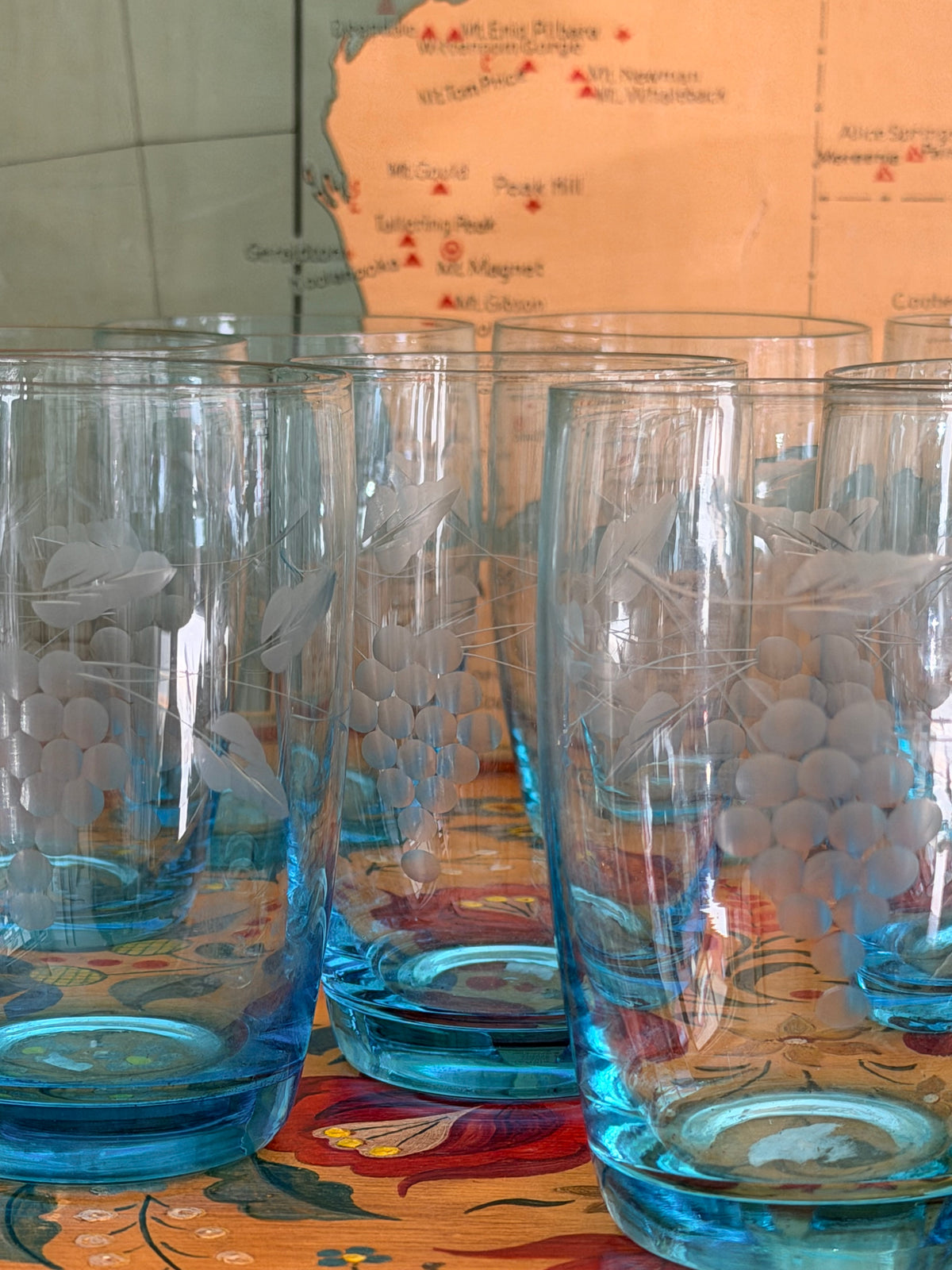 A group of retro vintage aqua blue glass tumblers with etched grape designs and bright blue bases,