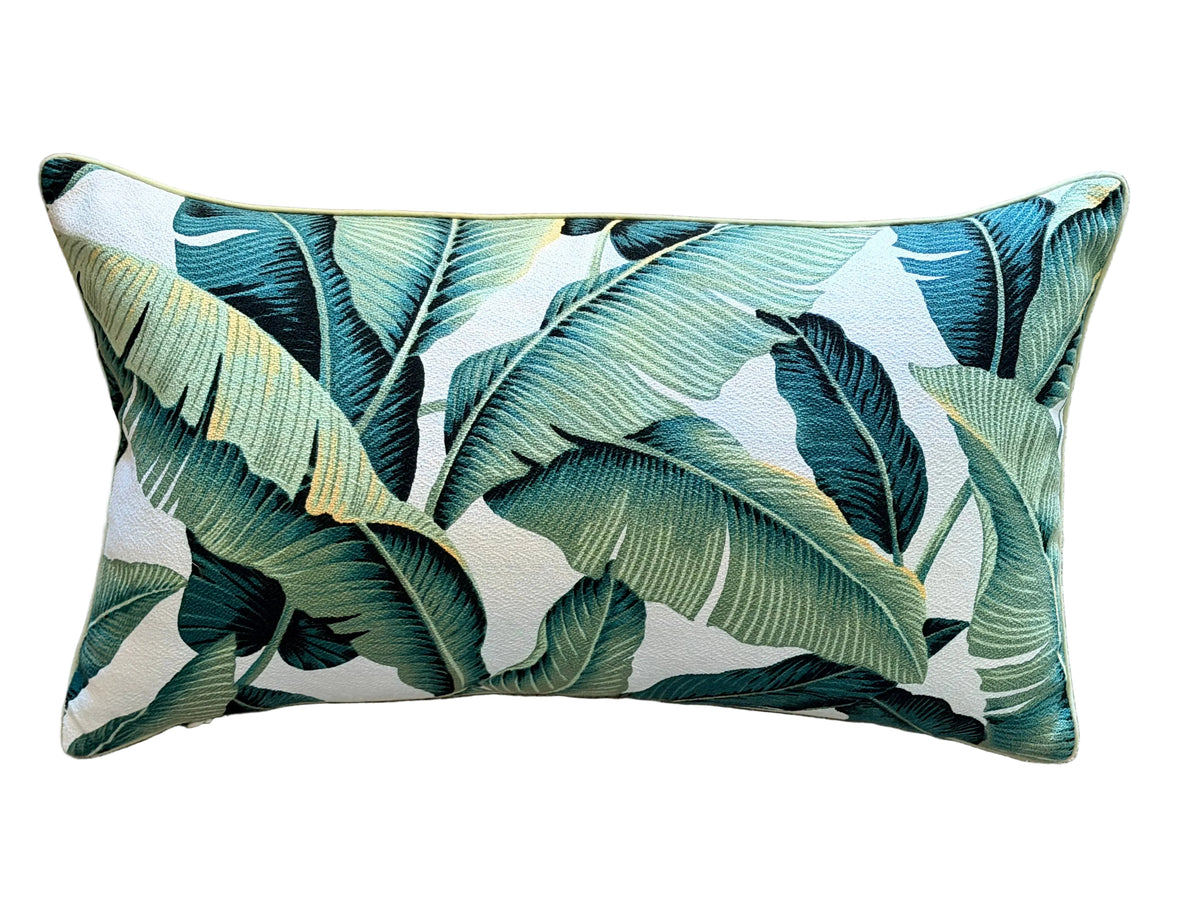 A rectangular lumbar throw pillow with a tropical banana leaf pattern in shades of green and teal on a white background