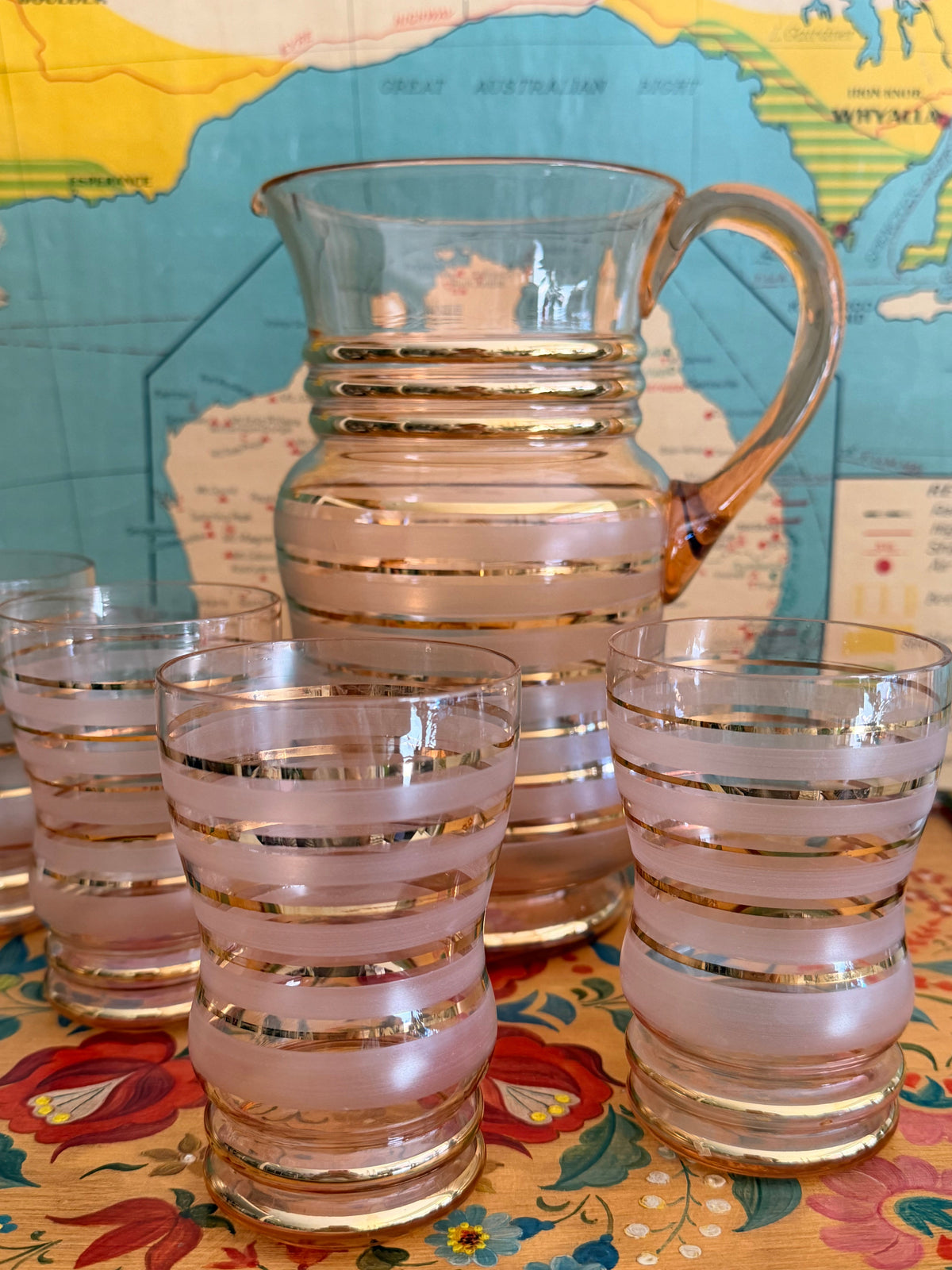 A vintage pink frosted glass pitcher and matching tumblers with gold metallic horizontal stripes