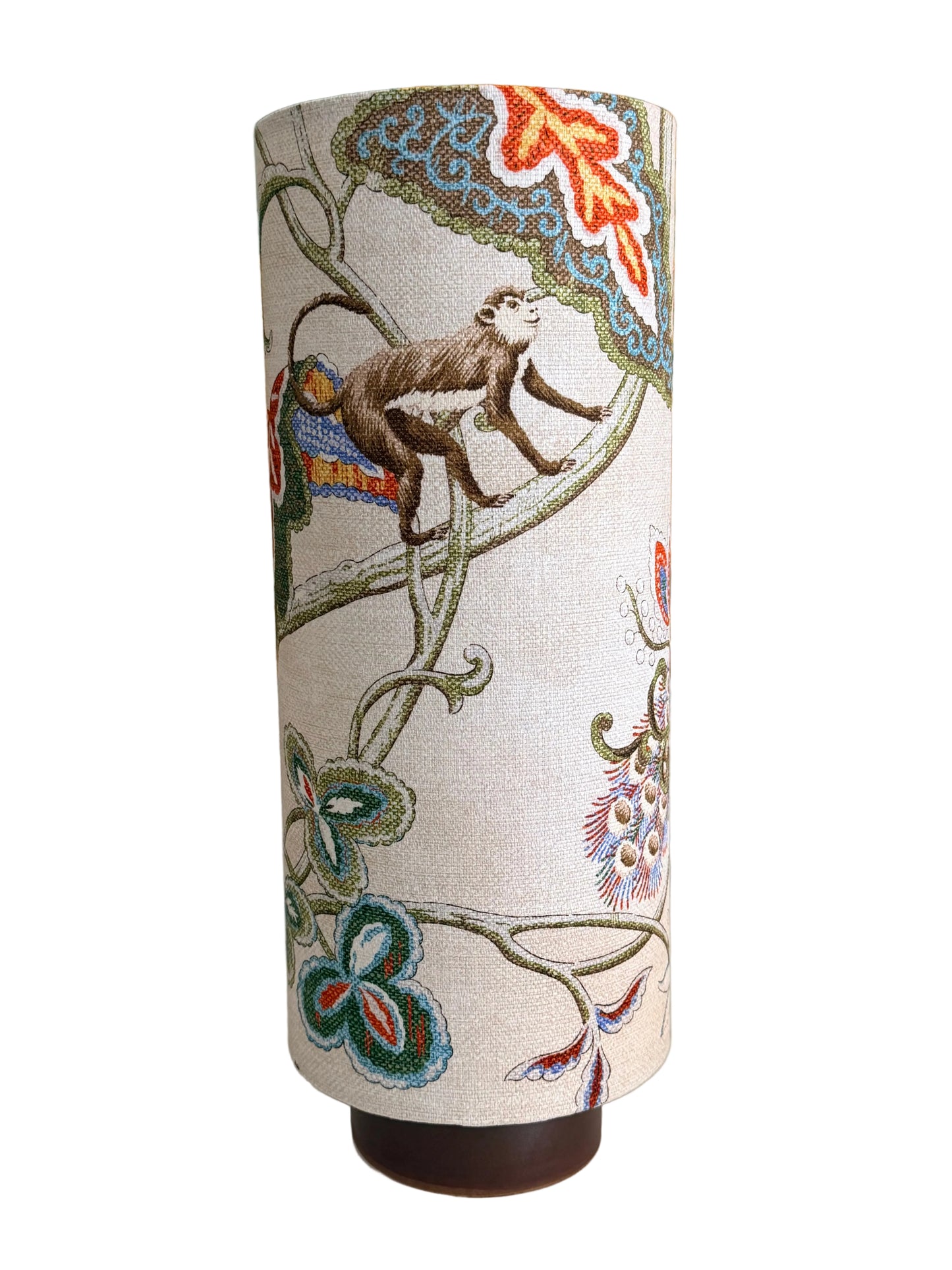 A cylindrical fabric-covered lampshade or vase cover featuring an embroidered design of a monkey climbing vines with floral motifs