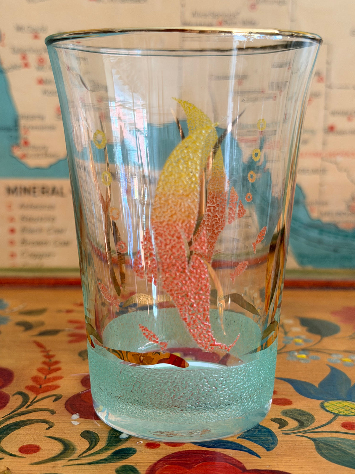 A  retro frosted pitcher with fotumblers, decorated with colorful fish illustrations in yellow, orange, and red and with a sea green frosted band