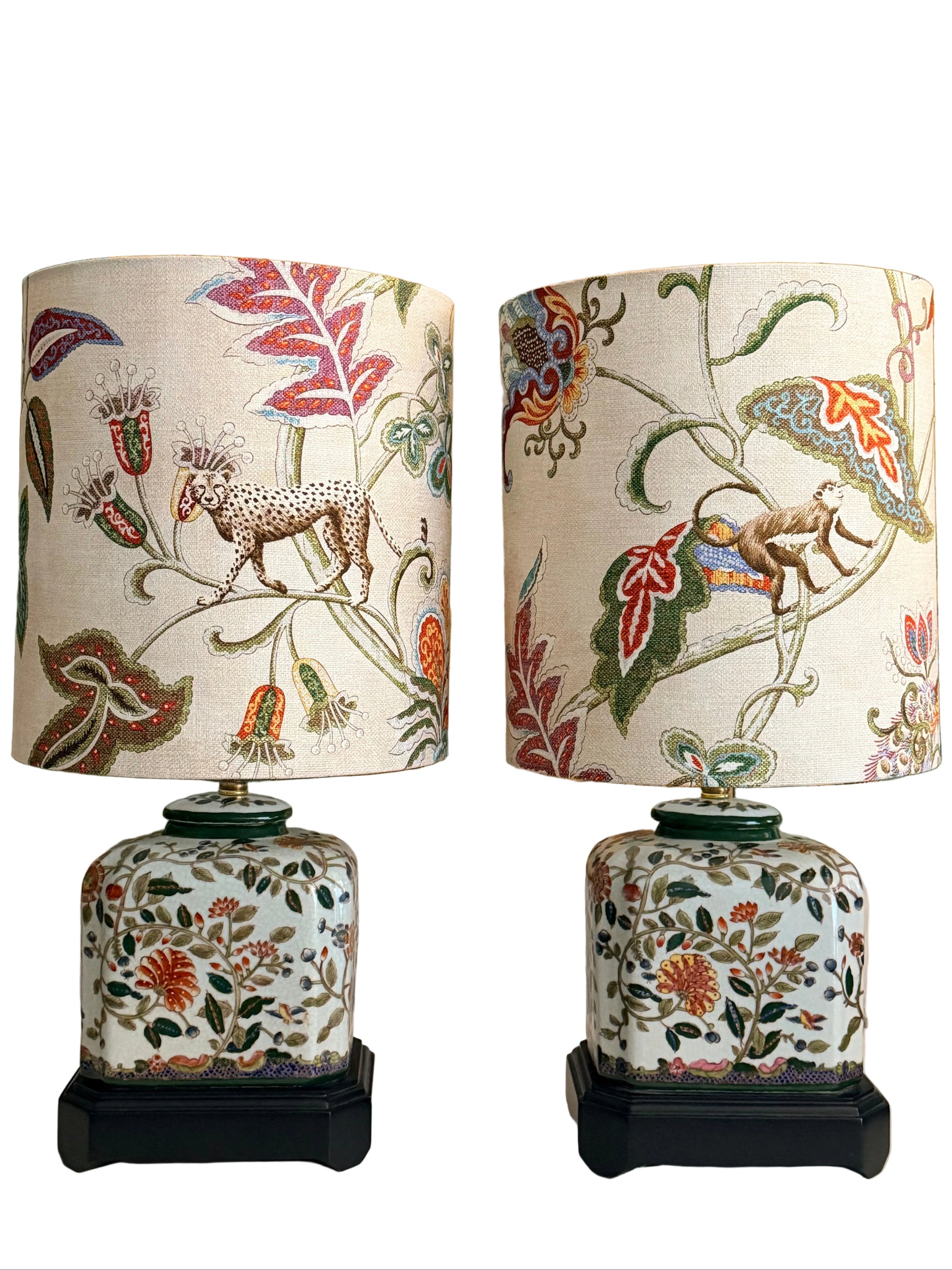 Two matching decorative table lamps with white patterned drum shades and white ceramic bases, displayed in front of a vintage-style map. The shades and bases feature multicolor floral and animal motifs including a leopard and a monkey.