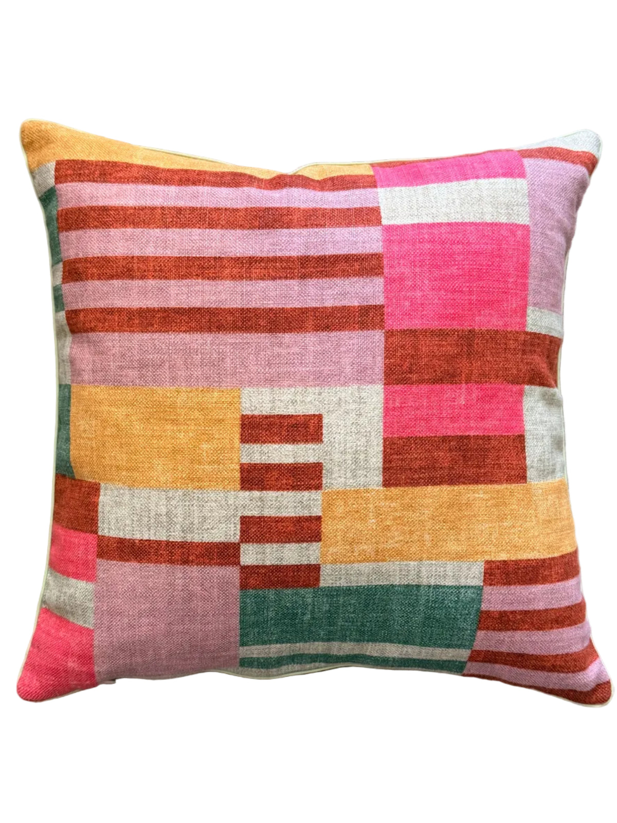 A square throw pillow with a colorful geometric patchwork pattern of pink, orange, yellow, green, and white textured fabric, resting on a beige woven rug.