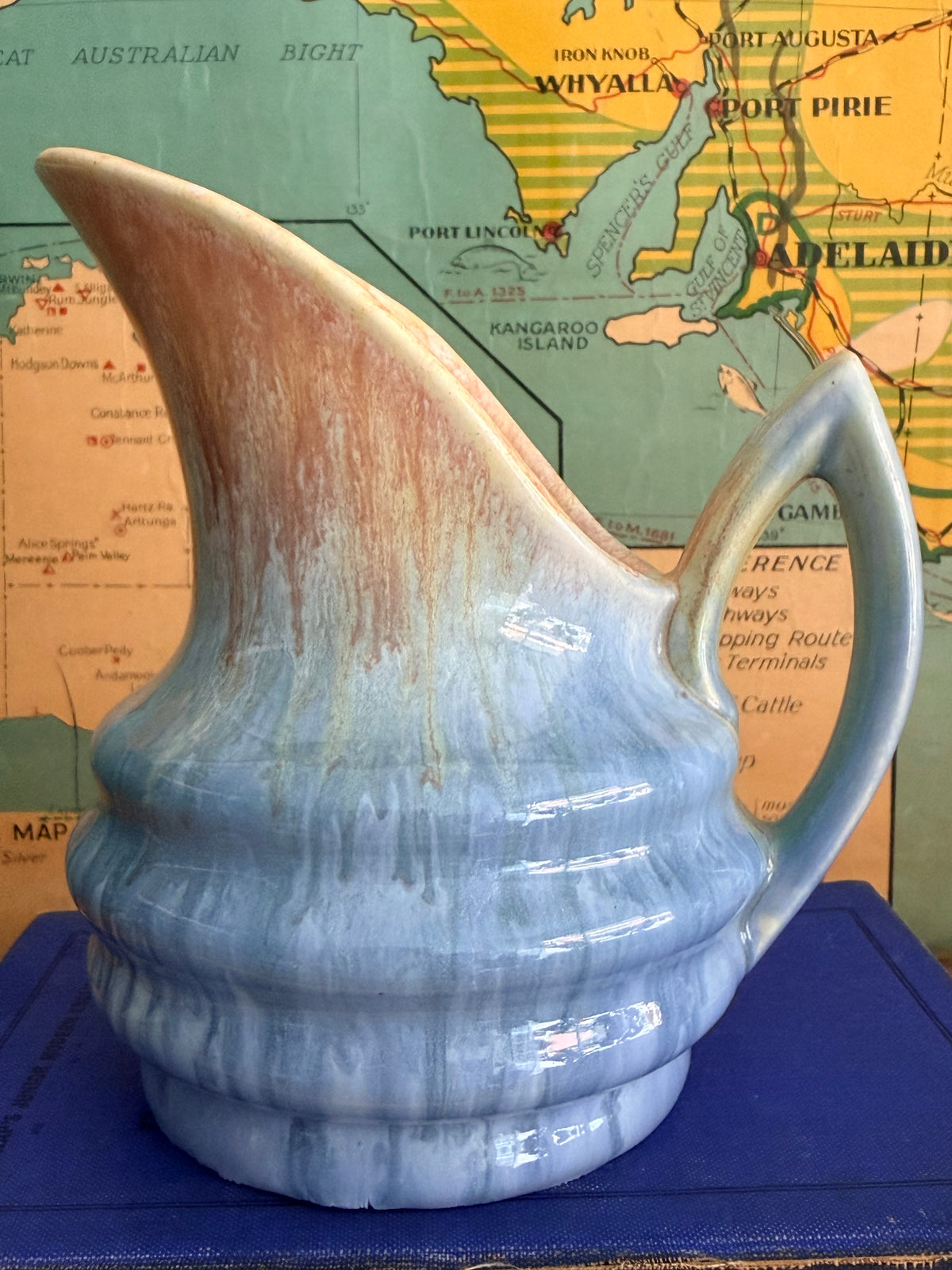 A small ceramic pitcher with a blue and beige marbled drip glaze