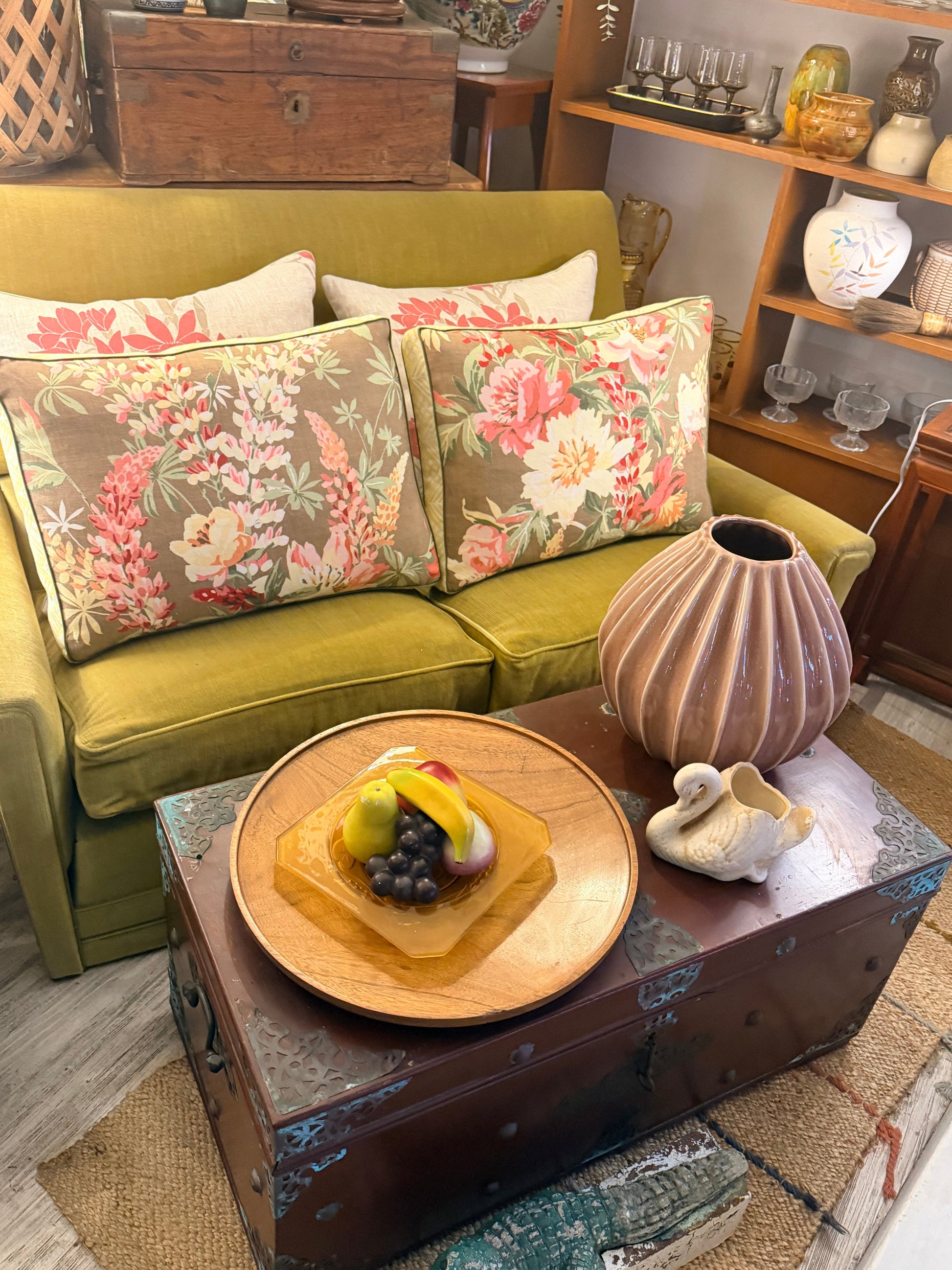 Green sofa with floral cushions, wooden coffee table with fruit plate, and decorative items in a room.