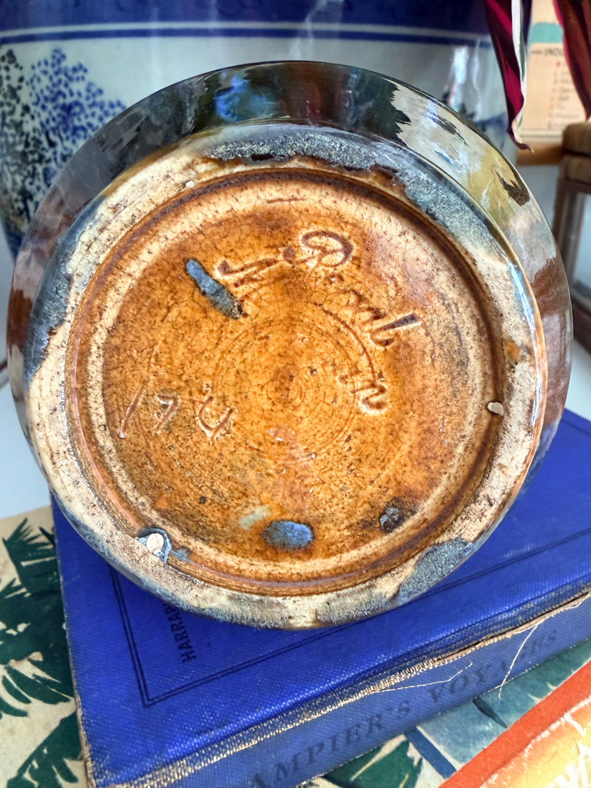 Close-up of the bottom of a round mashman ceramic plate or dish, showing a glossy brown and amber glaze with stamped maker's marks,
