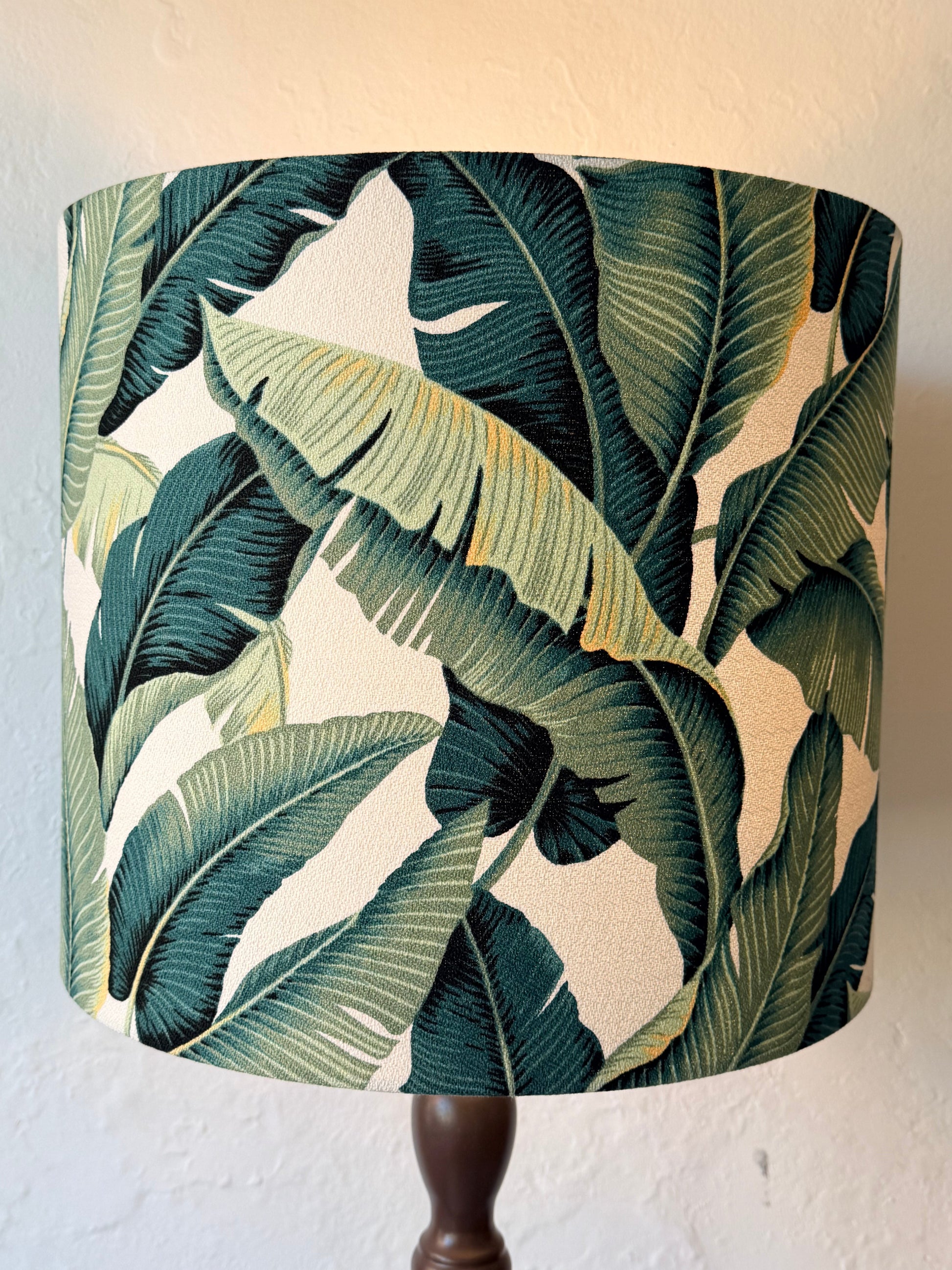 A lamp shade featuring a tropical banana leaf pattern in shades of green and white with dashes of yellow