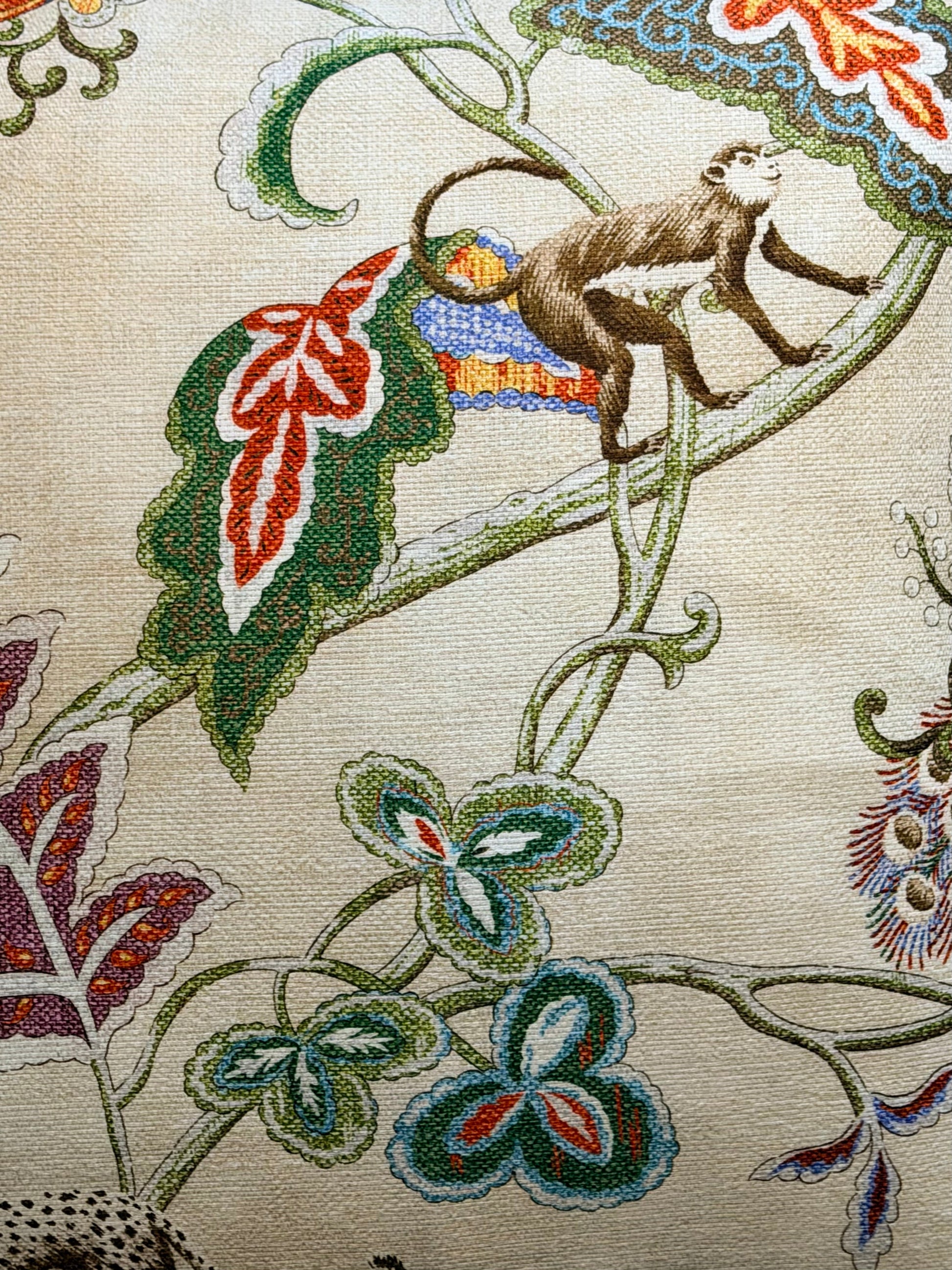 Close-up of a woven textile pattern featuring a brown monkey climbing on green vines with red, blue, and green leaves on a beige background.