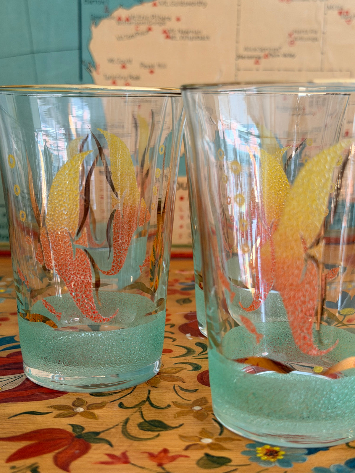 A  retro frosted pitcher with fotumblers, decorated with colorful fish illustrations in yellow, orange, and red and with a sea green frosted band